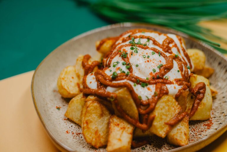 Patatas bravas con salsa y alioli en un plato de cerámica sobre fondo verde