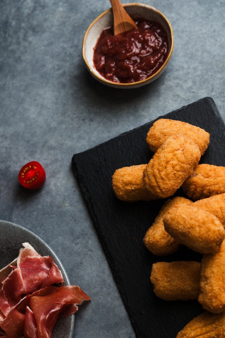 Croquetas con salsa y jamón sobre una pizarra