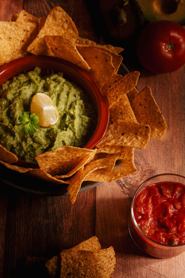Guacamole con nachos y salsa roja sobre una tabla de madera