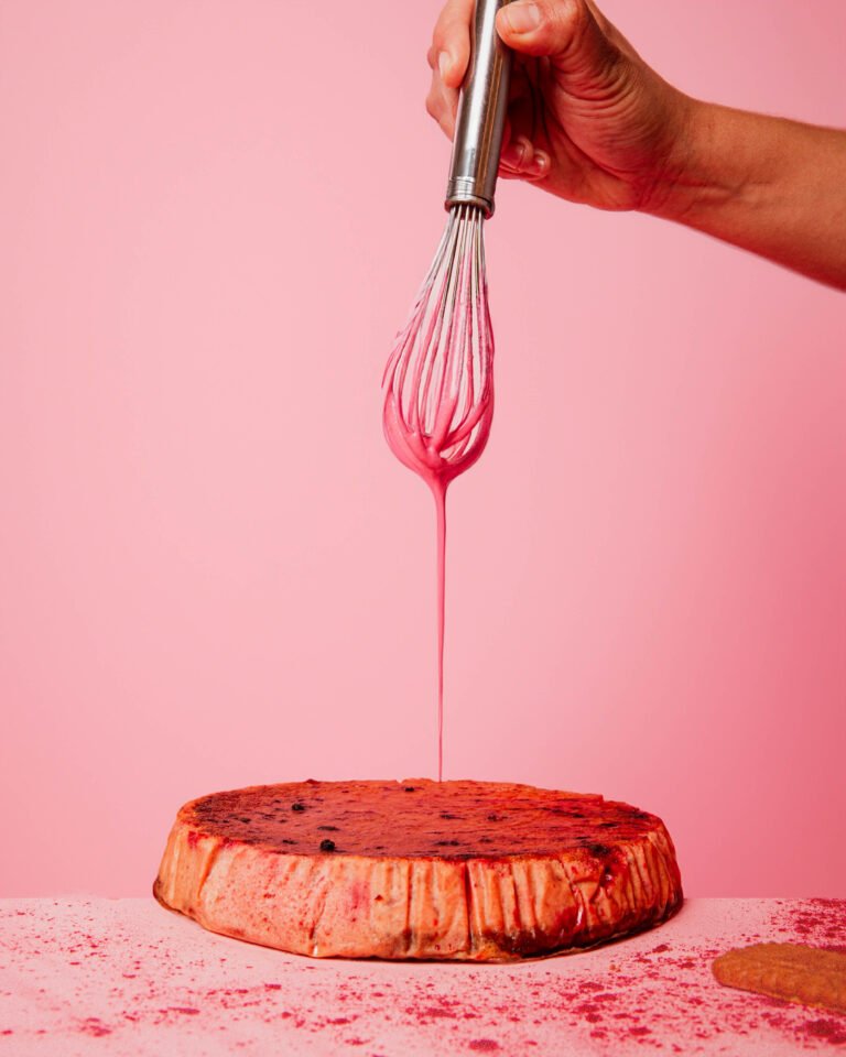 Mano vertiendo sirope rosa con una varilla sobre una tarta