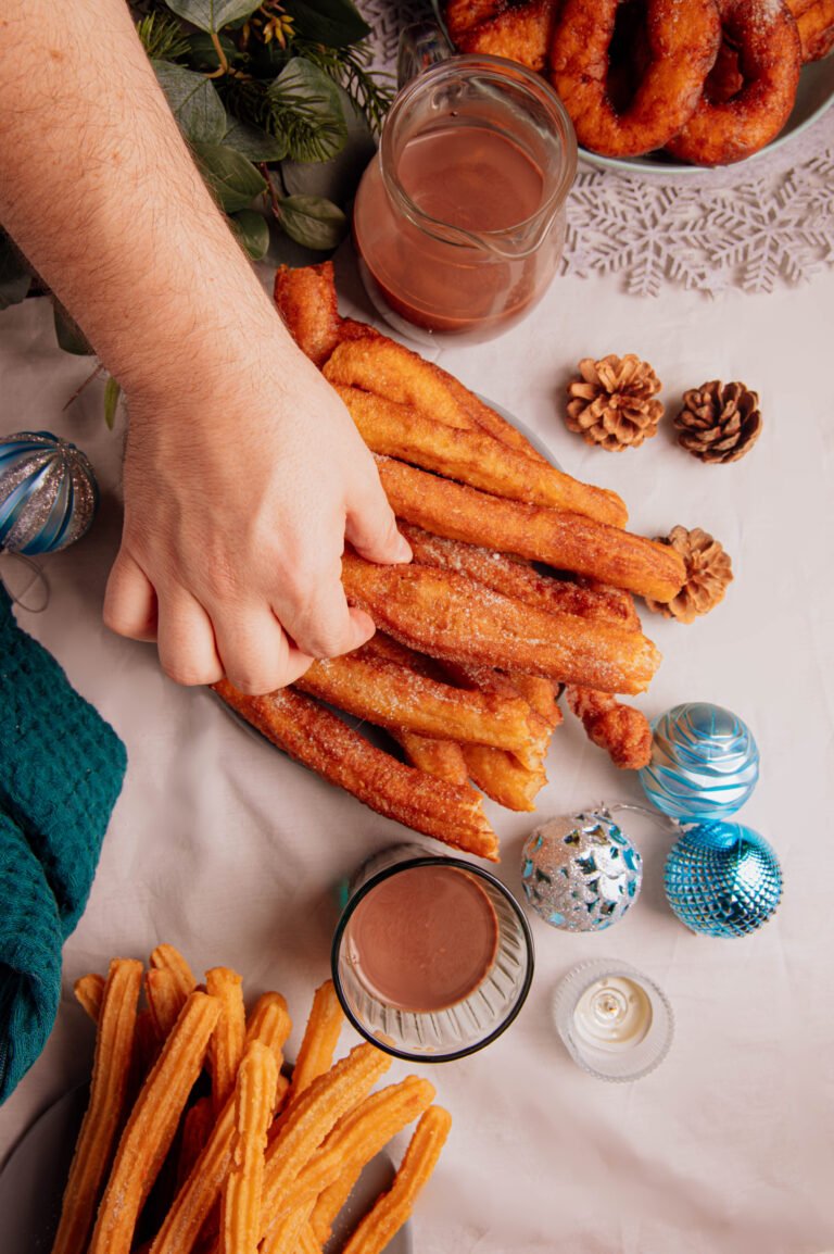 Manos sirviendo churros sobre una mesa