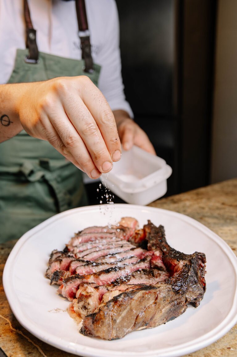 Mano añadiendo sal a un chuletón servido en un plato
